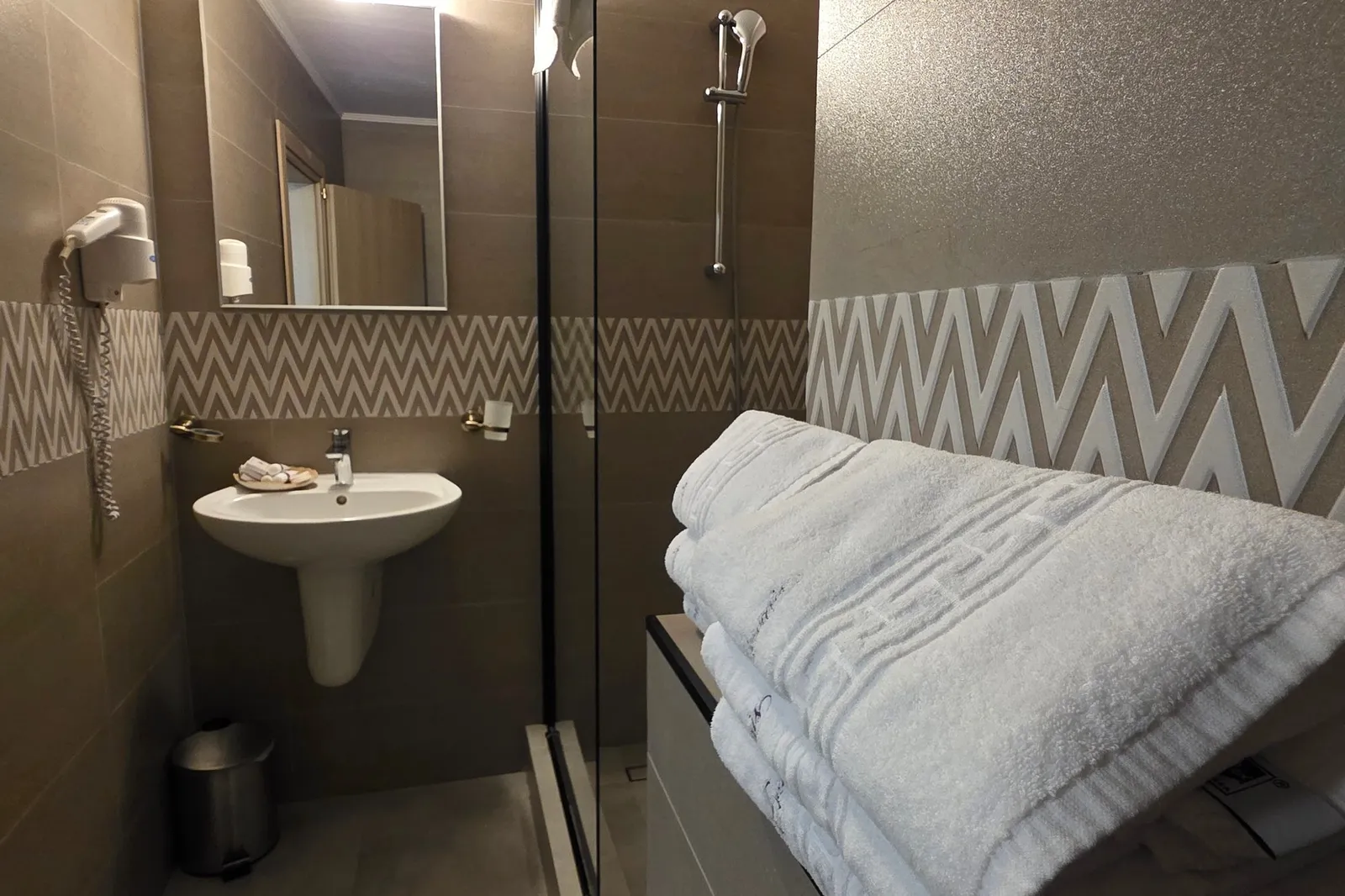 Embroidered towels in the foreground, with the basin and shower of the chevron-tiled bathroom